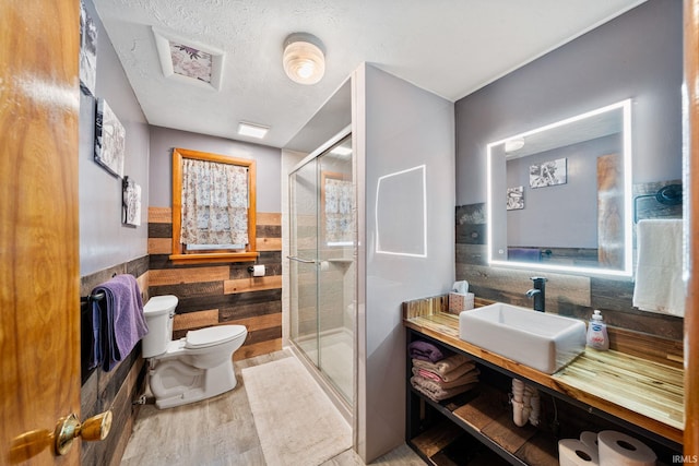 bathroom with a textured ceiling, hardwood / wood-style flooring, toilet, a shower with shower door, and vanity