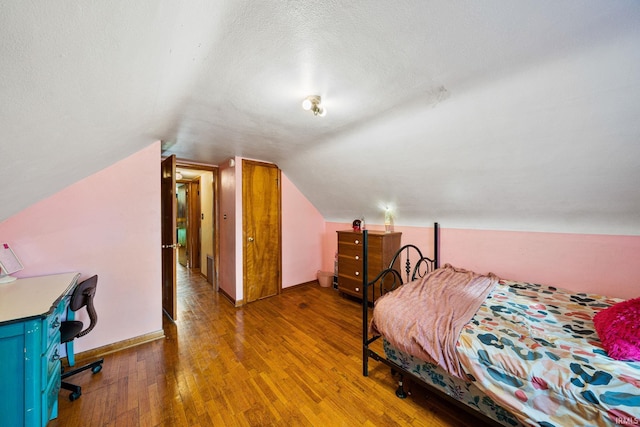 bedroom with hardwood / wood-style flooring, a textured ceiling, and lofted ceiling