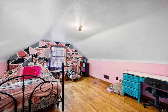 bedroom with lofted ceiling, light hardwood / wood-style flooring, and a textured ceiling