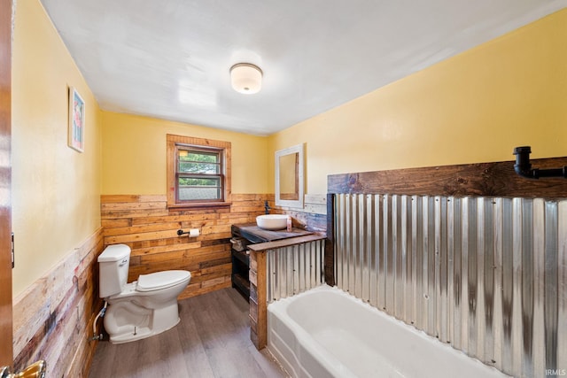 bathroom with hardwood / wood-style floors, toilet, wood walls, a washtub, and vanity