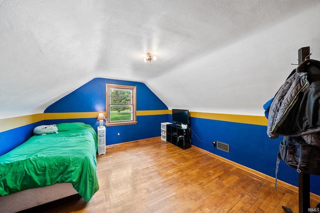 bedroom with vaulted ceiling, wood-type flooring, and a textured ceiling