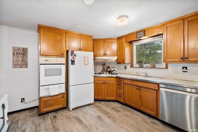 kitchen with white appliances, wood walls, sink, and light wood-type flooring