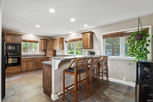 kitchen featuring black appliances, a wealth of natural light, kitchen peninsula, and a kitchen breakfast bar