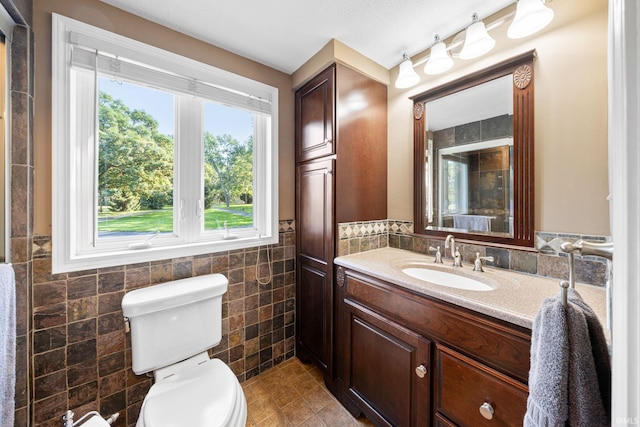 bathroom featuring toilet, tile patterned flooring, tile walls, vanity, and a textured ceiling