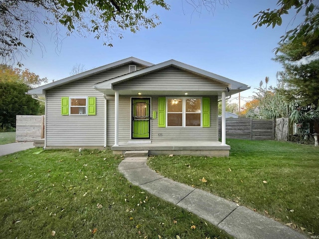 bungalow-style home with covered porch, fence, and a front lawn
