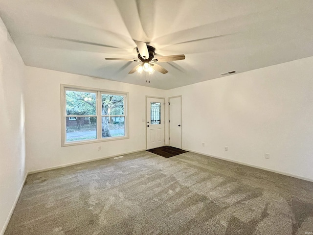 empty room featuring baseboards, visible vents, dark carpet, and ceiling fan