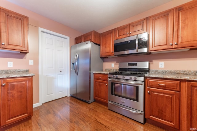 kitchen with appliances with stainless steel finishes, light stone counters, and light wood-type flooring