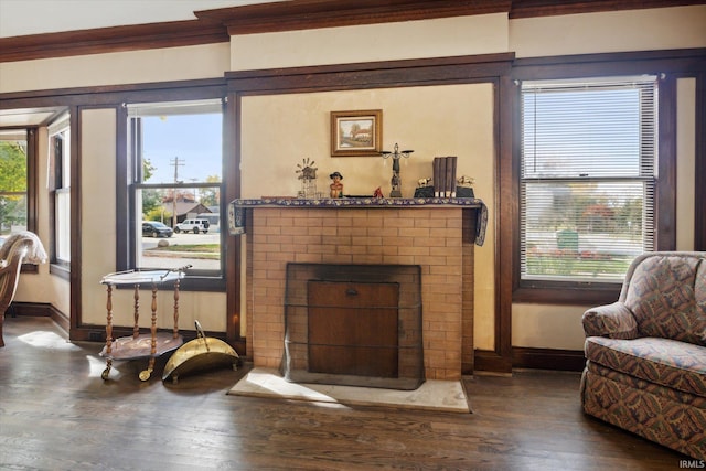 living room with dark wood-type flooring, crown molding, a wealth of natural light, and a brick fireplace