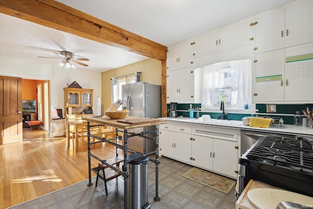 kitchen featuring white cabinets, ceiling fan, light wood-type flooring, beamed ceiling, and sink