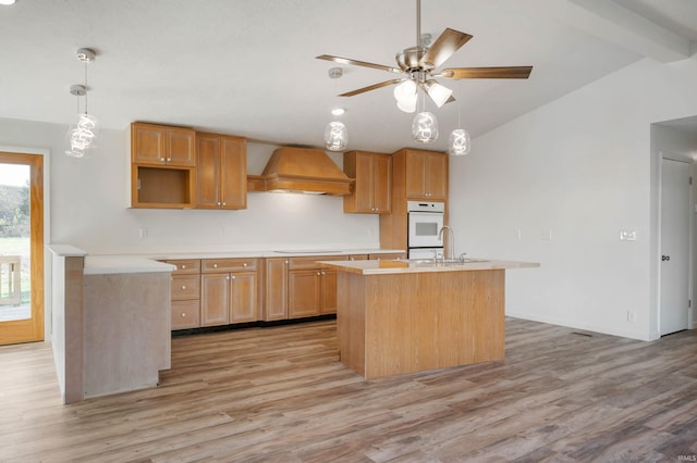 kitchen with custom exhaust hood, a center island with sink, ceiling fan, light hardwood / wood-style flooring, and lofted ceiling with beams