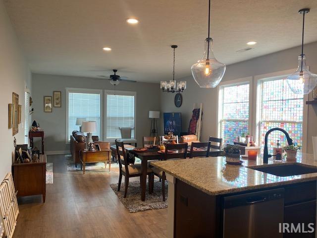 kitchen with wood-type flooring, sink, dishwasher, an island with sink, and ceiling fan with notable chandelier