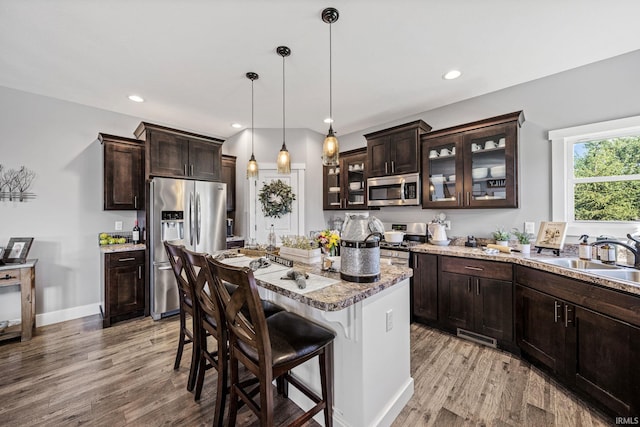 kitchen with a breakfast bar area, stainless steel appliances, sink, light hardwood / wood-style floors, and a center island