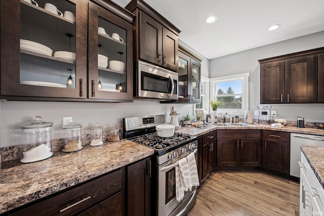 kitchen featuring dark brown cabinets, appliances with stainless steel finishes, light stone countertops, light hardwood / wood-style floors, and sink