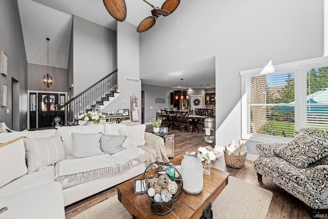 living room with hardwood / wood-style floors, ceiling fan with notable chandelier, and a towering ceiling