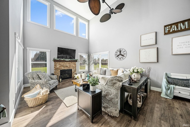 living room with a towering ceiling, ceiling fan, wood-type flooring, and a fireplace