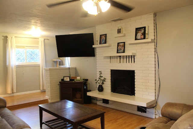 living room featuring a brick fireplace, ceiling fan, and light wood-type flooring