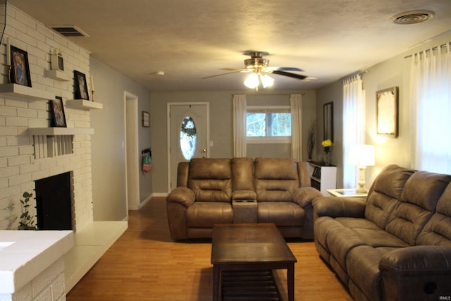 living room featuring ceiling fan, light wood-type flooring, and a brick fireplace