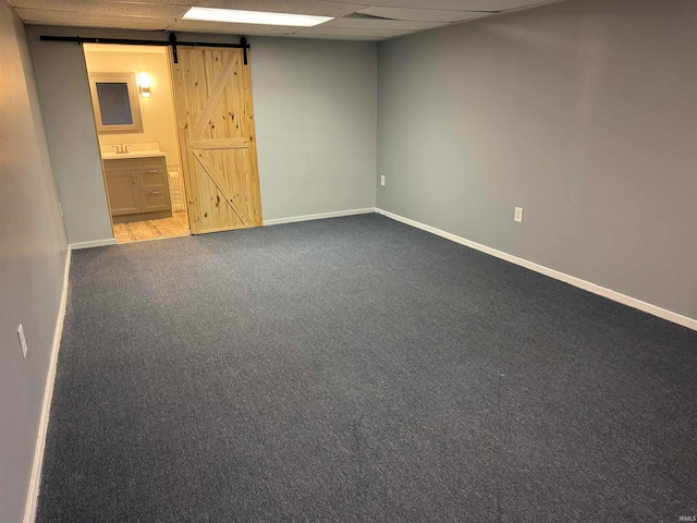 empty room with sink, a drop ceiling, a barn door, and light colored carpet