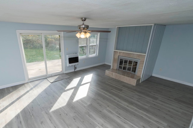 unfurnished living room with a fireplace, a textured ceiling, ceiling fan, heating unit, and hardwood / wood-style flooring