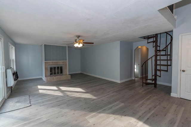 unfurnished living room with light hardwood / wood-style flooring, a tiled fireplace, heating unit, and ceiling fan