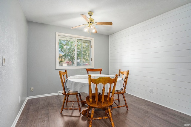 dining space featuring wood walls, dark wood-type flooring, a textured ceiling, and ceiling fan