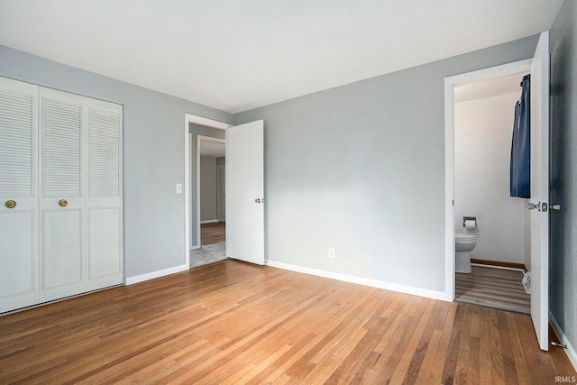 unfurnished bedroom featuring a closet, ensuite bathroom, and hardwood / wood-style flooring