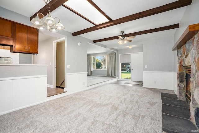 unfurnished living room featuring beamed ceiling, light carpet, a fireplace, and ceiling fan with notable chandelier