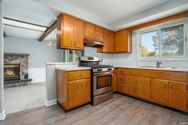 kitchen featuring light wood-type flooring, beamed ceiling, stainless steel gas stove, a stone fireplace, and sink