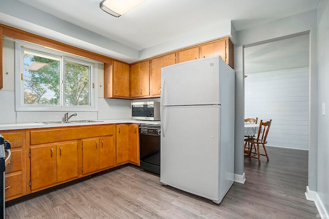 kitchen with black dishwasher, wood walls, sink, light hardwood / wood-style flooring, and white refrigerator