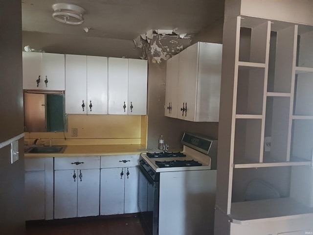 kitchen featuring white gas range oven, sink, and white cabinets