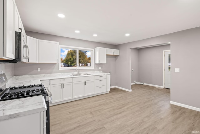 kitchen featuring light stone countertops, range with gas cooktop, sink, light wood-type flooring, and white cabinets