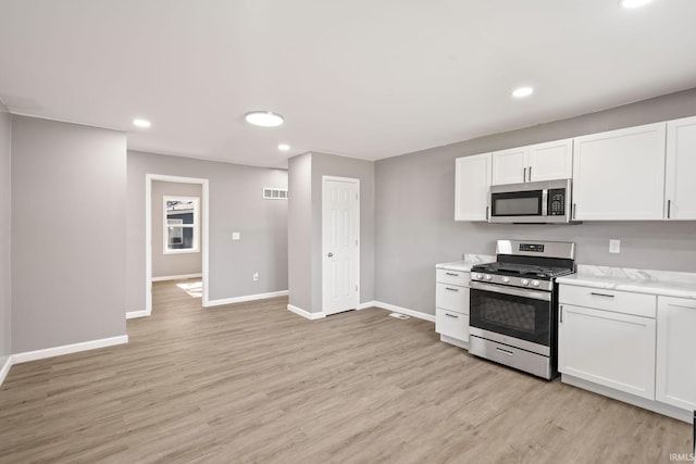 kitchen with appliances with stainless steel finishes, light hardwood / wood-style flooring, white cabinets, and light stone countertops