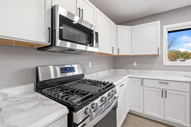 kitchen featuring appliances with stainless steel finishes, white cabinetry, light stone countertops, and light hardwood / wood-style floors