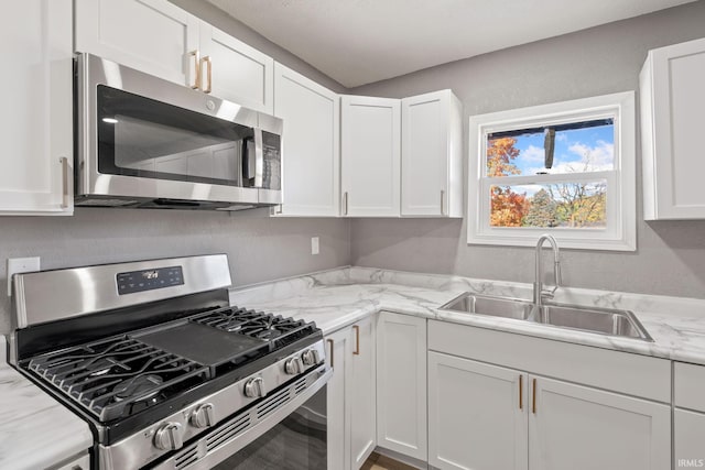 kitchen with white cabinetry, light stone countertops, stainless steel appliances, and sink