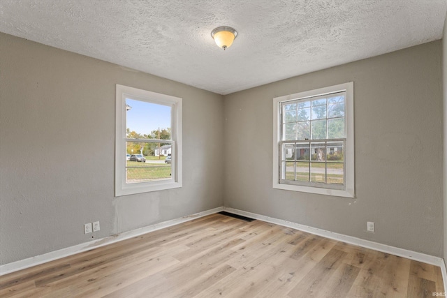 spare room with light wood-type flooring, a textured ceiling, and plenty of natural light