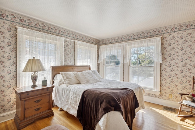 bedroom with baseboards, wallpapered walls, and light wood-style floors
