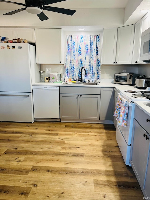 kitchen featuring white appliances, sink, white cabinetry, light hardwood / wood-style floors, and ceiling fan