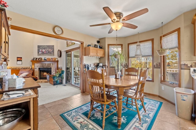 dining area featuring ceiling fan, a stone fireplace, a textured ceiling, and light tile patterned floors