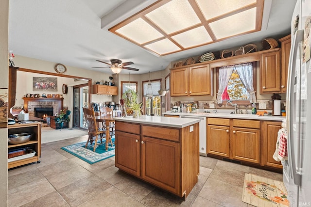 kitchen with ceiling fan, dishwasher, sink, a fireplace, and a center island