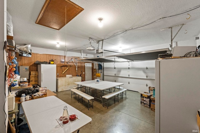 garage featuring a garage door opener, white fridge, and wooden walls