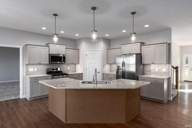 kitchen with an island with sink, appliances with stainless steel finishes, sink, dark wood-type flooring, and decorative light fixtures