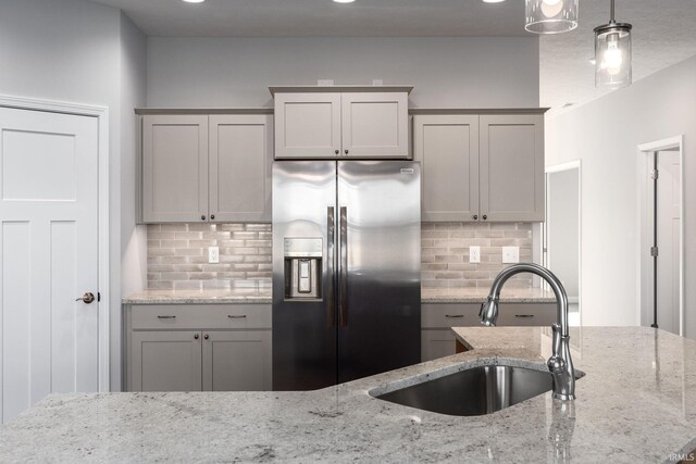 kitchen with tasteful backsplash, stainless steel fridge with ice dispenser, light stone countertops, gray cabinets, and sink