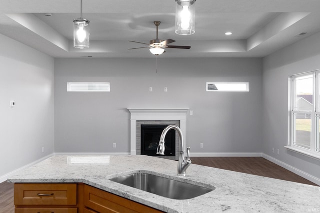 kitchen featuring light stone countertops, sink, a fireplace, hanging light fixtures, and dark wood-type flooring