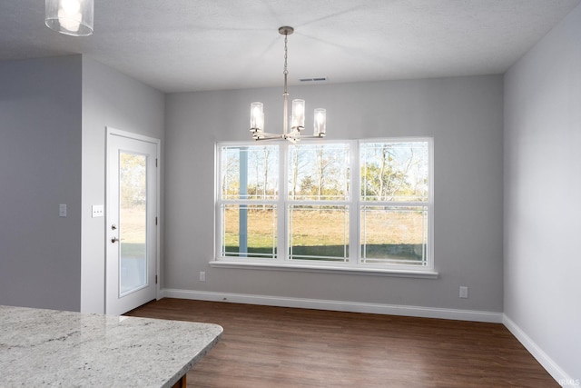 unfurnished dining area featuring a textured ceiling, a healthy amount of sunlight, and dark wood-type flooring