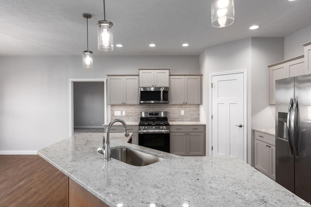 kitchen with light stone countertops, appliances with stainless steel finishes, sink, dark hardwood / wood-style flooring, and pendant lighting