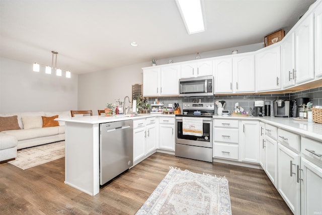 kitchen featuring kitchen peninsula, stainless steel appliances, pendant lighting, white cabinets, and dark wood-type flooring