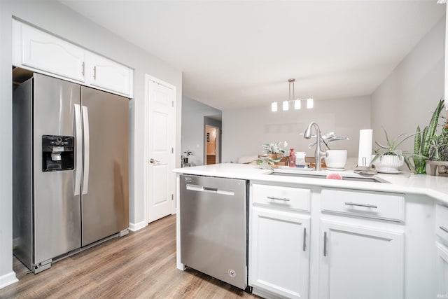 kitchen with hanging light fixtures, stainless steel appliances, sink, white cabinets, and light hardwood / wood-style floors