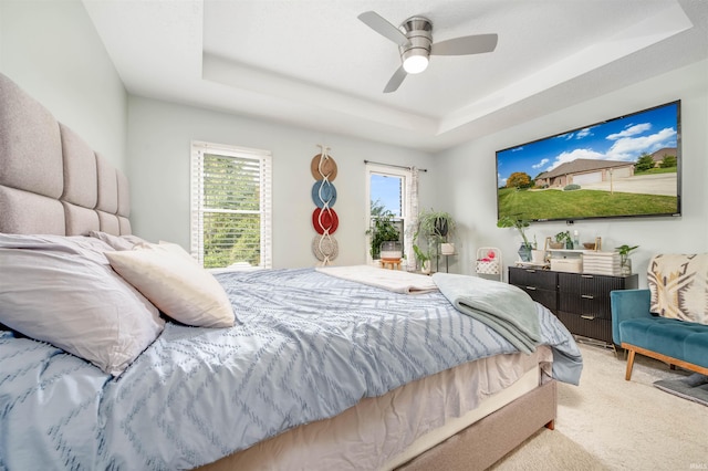 carpeted bedroom with ceiling fan and a raised ceiling