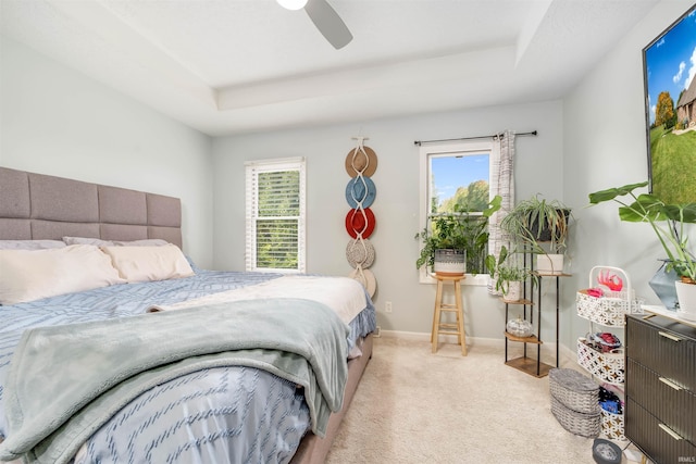 bedroom with light colored carpet, a tray ceiling, and ceiling fan