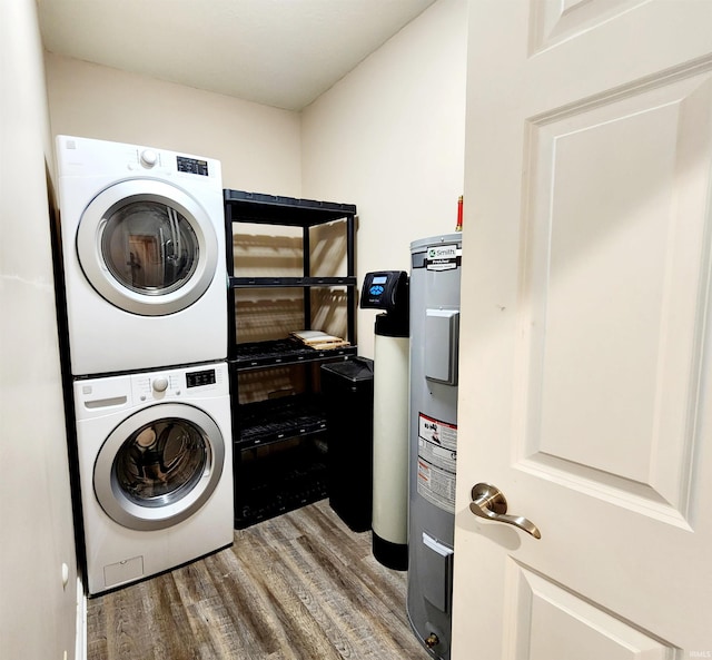 clothes washing area with stacked washing maching and dryer, hardwood / wood-style flooring, and water heater